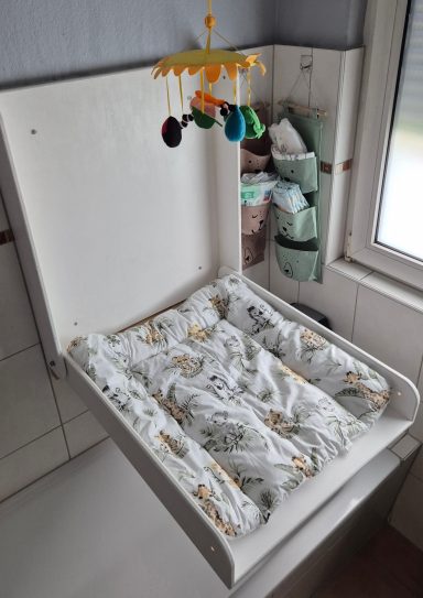 Wickelkommode mit einem bunten Spiele-Mobile und einem gestreiften Wickelauflagenbezug.