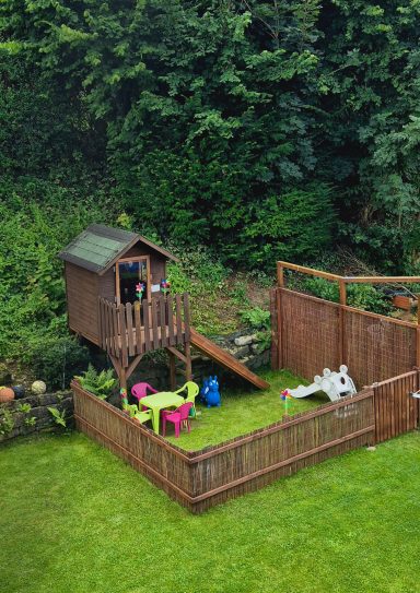 Spielplatz mit Spielhaus, Rutsche und bunten Gartenmöbeln in einem umzäunten Garten.