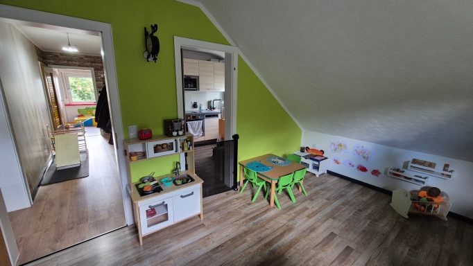 Bunte Spielecke mit Tisch und Stühlen in einem hellen Raum mit grüner Wand.