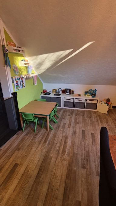 Spielzimmer unter dem Dach mit Tisch, Stühlen und bunten Spielzeugen.